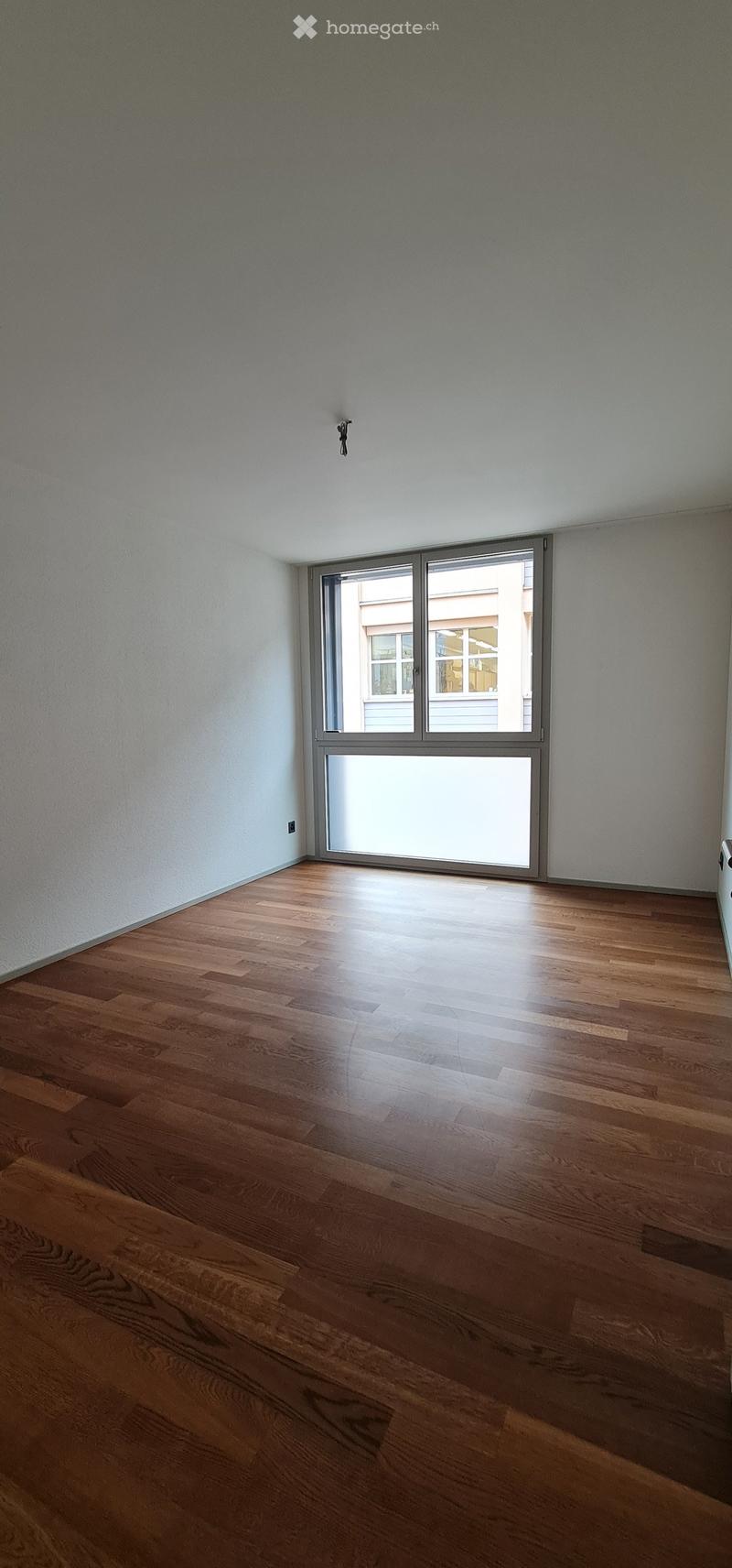 Empty room with wooden flooring and large sliding glass door leading to a view of another building.