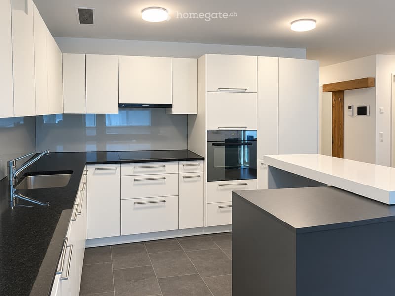 Modern kitchen with white cabinets, stainless steel sink, and built-in oven. Features a dark countertop and tiled floor.