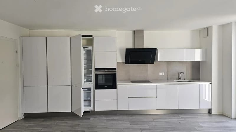 Modern kitchen with white cabinets, stainless steel appliances, and a wooden floor.