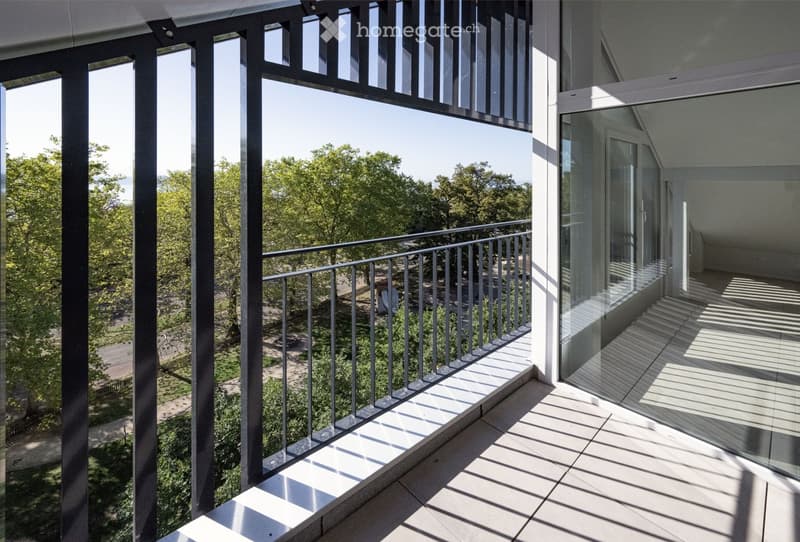 Modern balcony with glass railing, tiled floor, and a view of a green park area with trees and pathways.