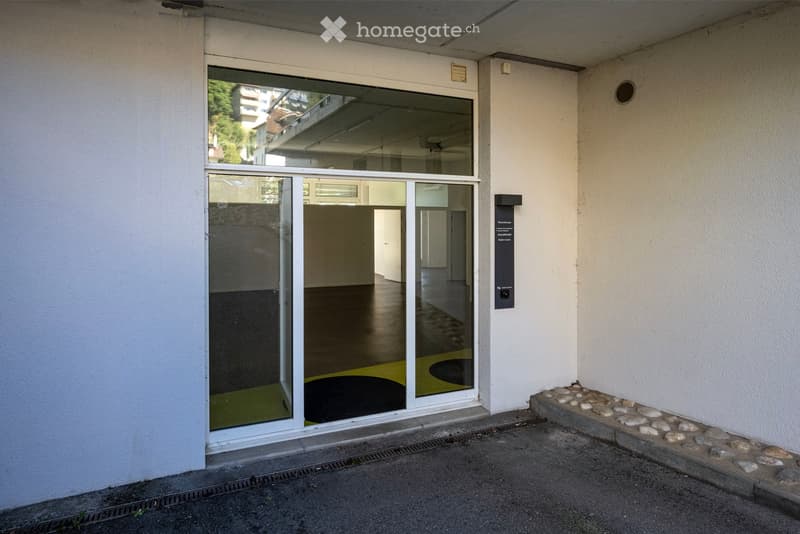 Entrance to a building with large glass doors, a raised ground floor, and a small stone border along the edge.