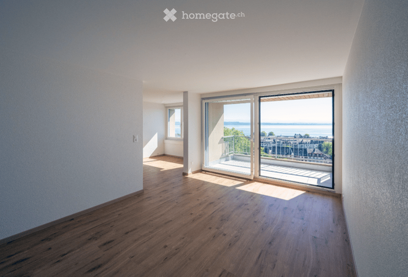 Empty room with wooden flooring, large sliding glass doors leading to a balcony with a scenic view of the water and surrounding buildings.