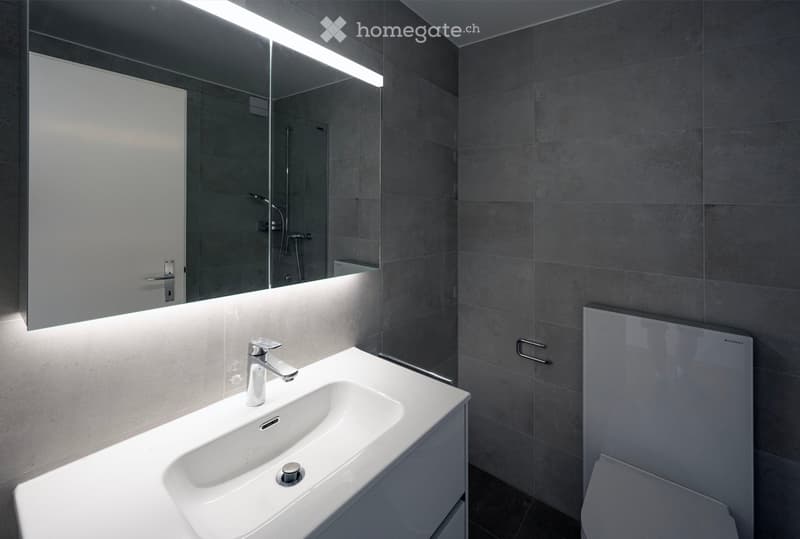 Modern bathroom with a white sink, chrome faucet, large mirror with built-in lighting, and a toilet.
