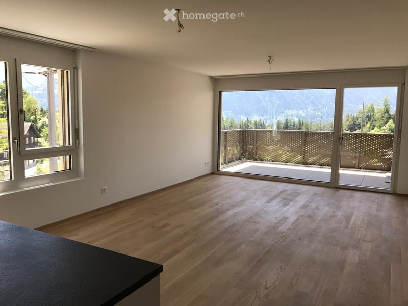 Empty room with wooden flooring, large windows, and sliding doors leading to a balcony with a scenic mountain view.