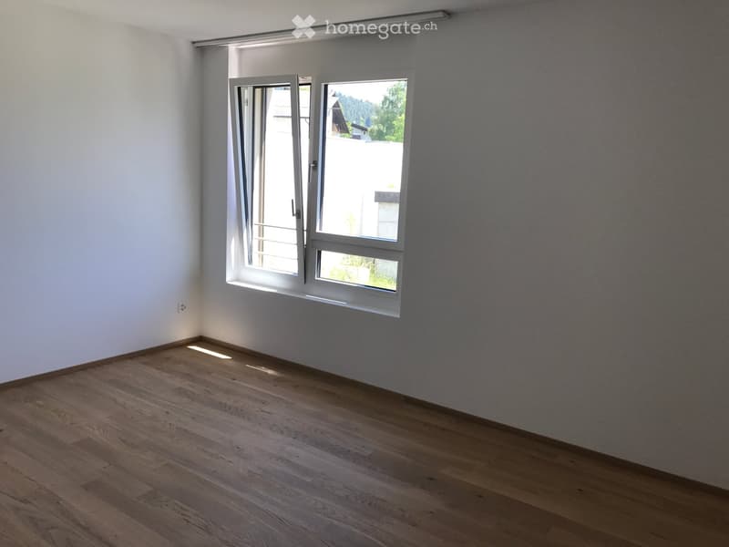 Empty room with wooden flooring, white walls, and large windows with blinds.
