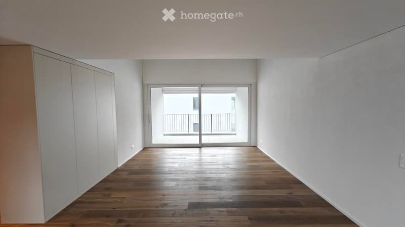 Empty room with wooden flooring, white walls, and a sliding glass door leading to a balcony.
