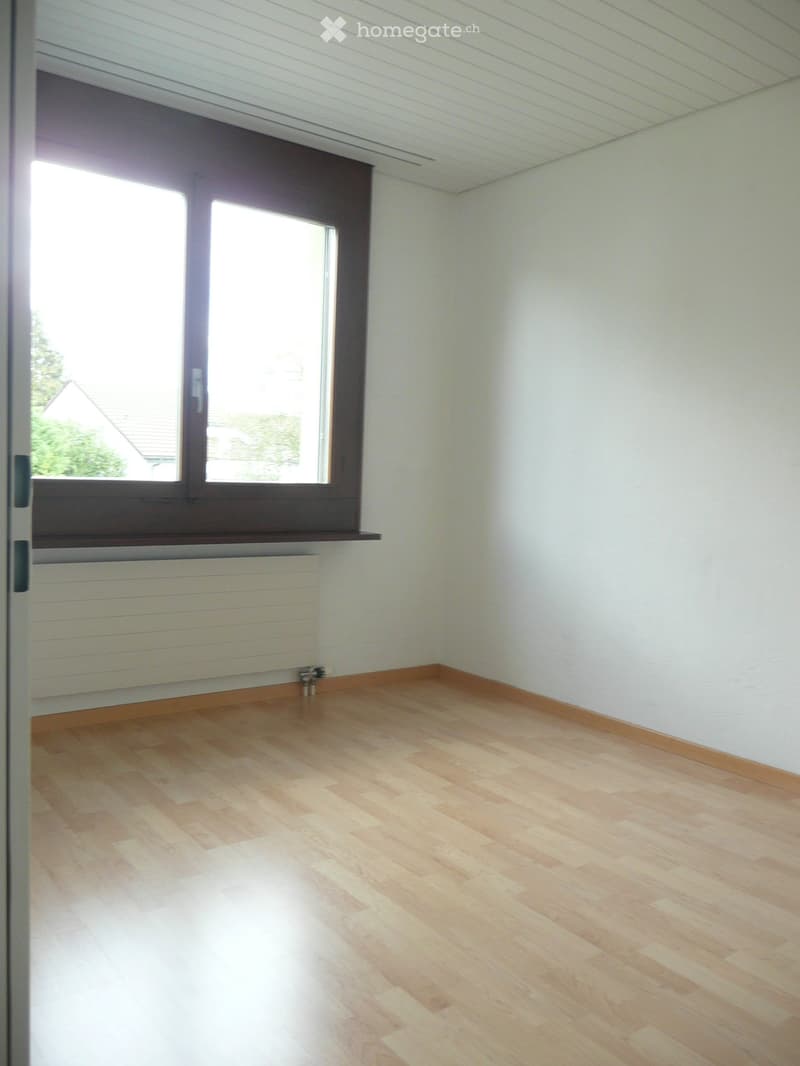 Empty room with light wooden flooring, white walls, and a large window with a radiator below it.
