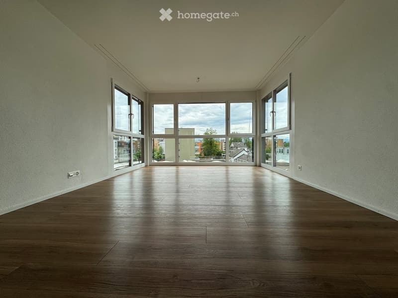 Empty room with wooden flooring and large windows offering a view of the outside. The walls are painted a light color, and the space is well-lit with natural light.