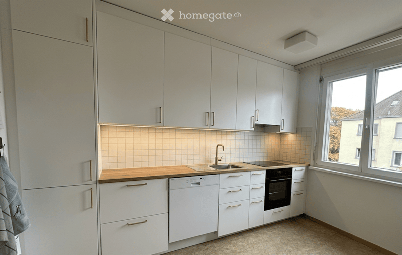 Modern kitchen with white cabinets, wooden countertop, sink, faucet, oven, and dishwasher. Light-colored tiles on backsplash and a window offering a view of the outside.