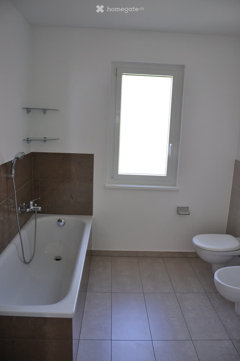 Modern bathroom with a bathtub, toilet, showerhead, and shelves, featuring tiled floors and walls.