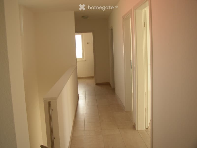 Empty hallway with tiled floor, white walls, and several doors leading to rooms.