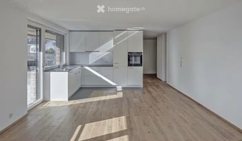 Modern kitchen with white cabinets, wooden flooring, and large windows allowing natural light to fill the space.