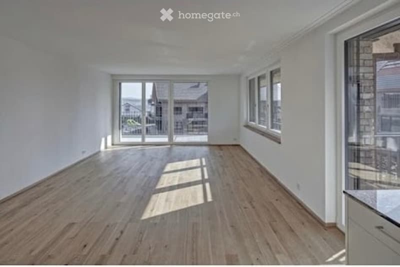 Bright, empty room with wooden flooring, large windows, and sliding glass doors leading to an outdoor area.