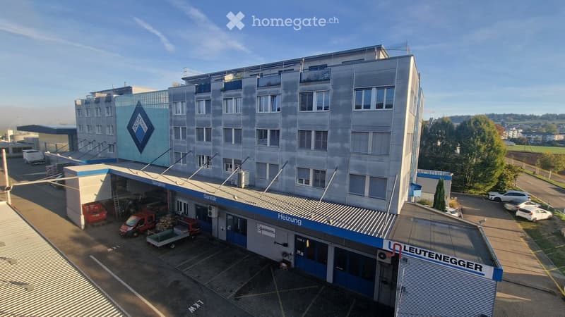 Modern multi-story building with a garage area, several parked vehicles, and a clear blue sky in the background.