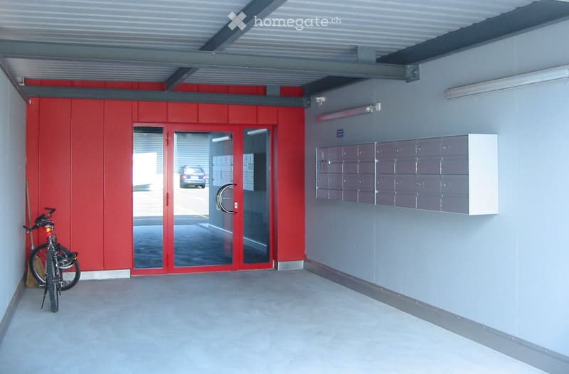 A modern, clean entrance area with a red door, mailboxes, and a bicycle leaning against the wall.