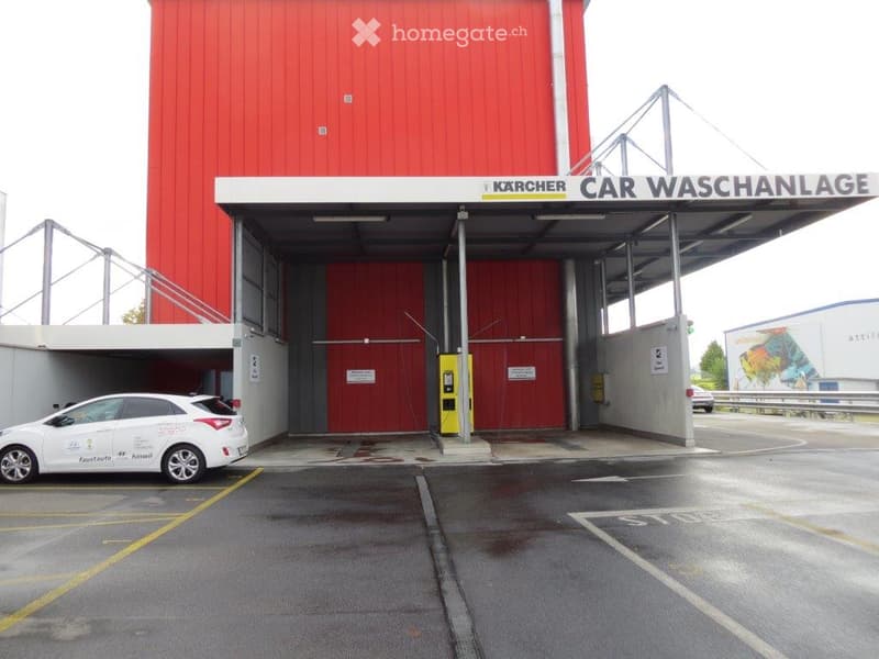 Car wash facility with a large red building, garage entrance, and a white car parked nearby.