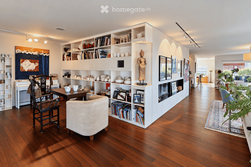 Modern living room with hardwood floors, large built-in bookshelf, sofa, armchair, coffee table, decorative art, and plants.