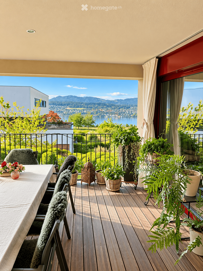 Balcony with wooden decking, table, chairs, potted plants, and scenic view of a lake and mountains.