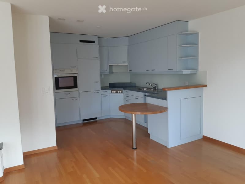 Modern kitchen with light blue cabinets, stainless steel appliances, wooden countertop, and a round wooden table with a metal base.