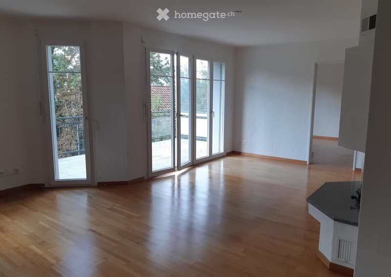 Empty room with wooden flooring, large windows, and sliding glass doors leading to a balcony.