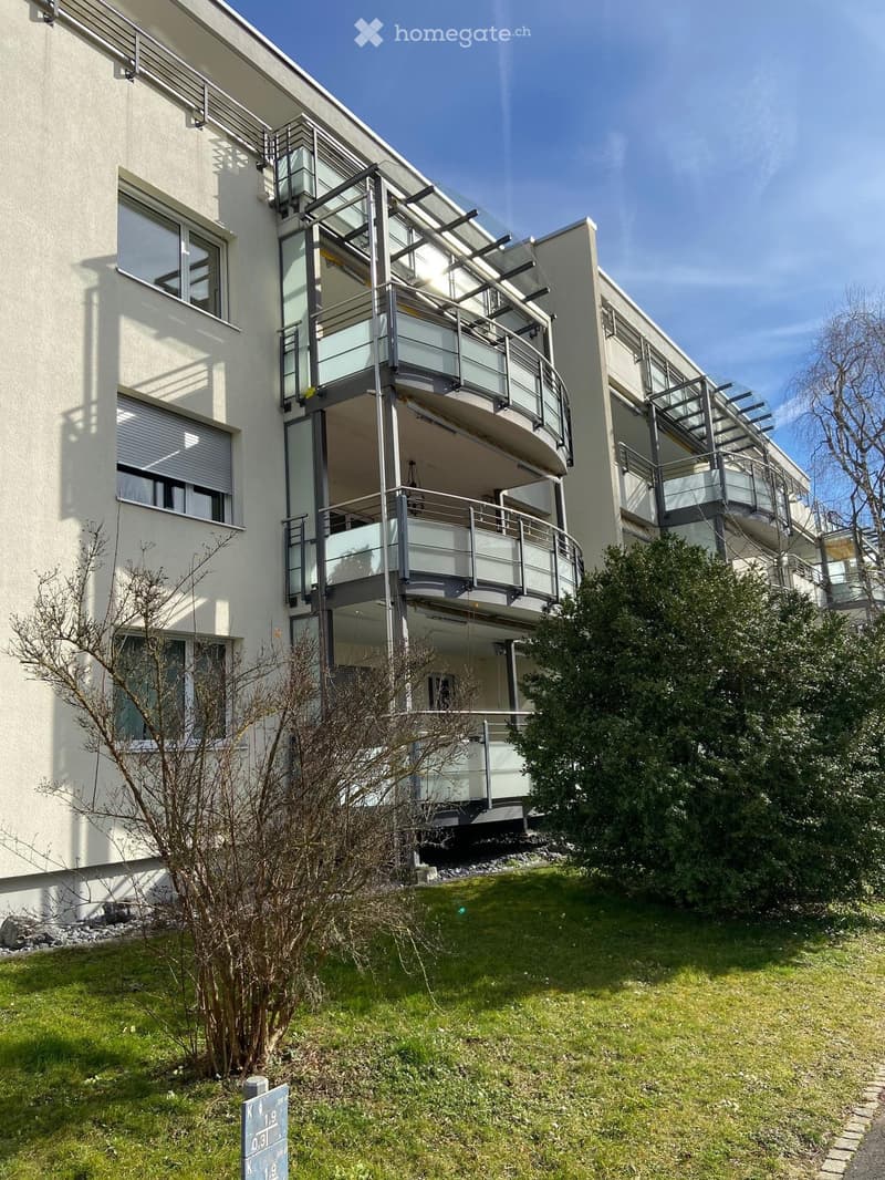 Modern multi-story building with balconies, white exterior, and glass windows.