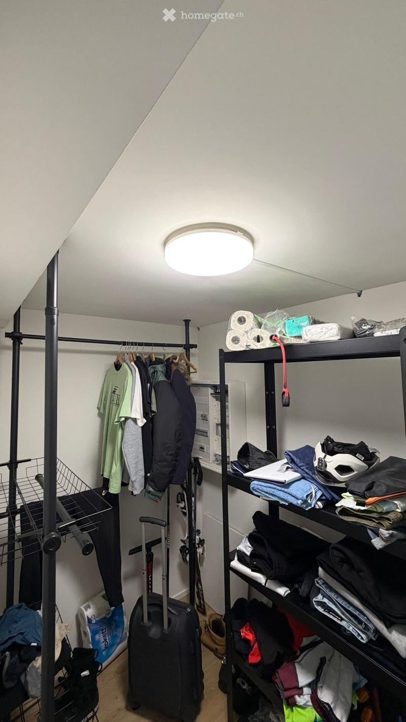 A well-organized closet with a clothing rack, shelves filled with folded clothes, a suitcase on the floor, and various storage items including toilet paper and skis.