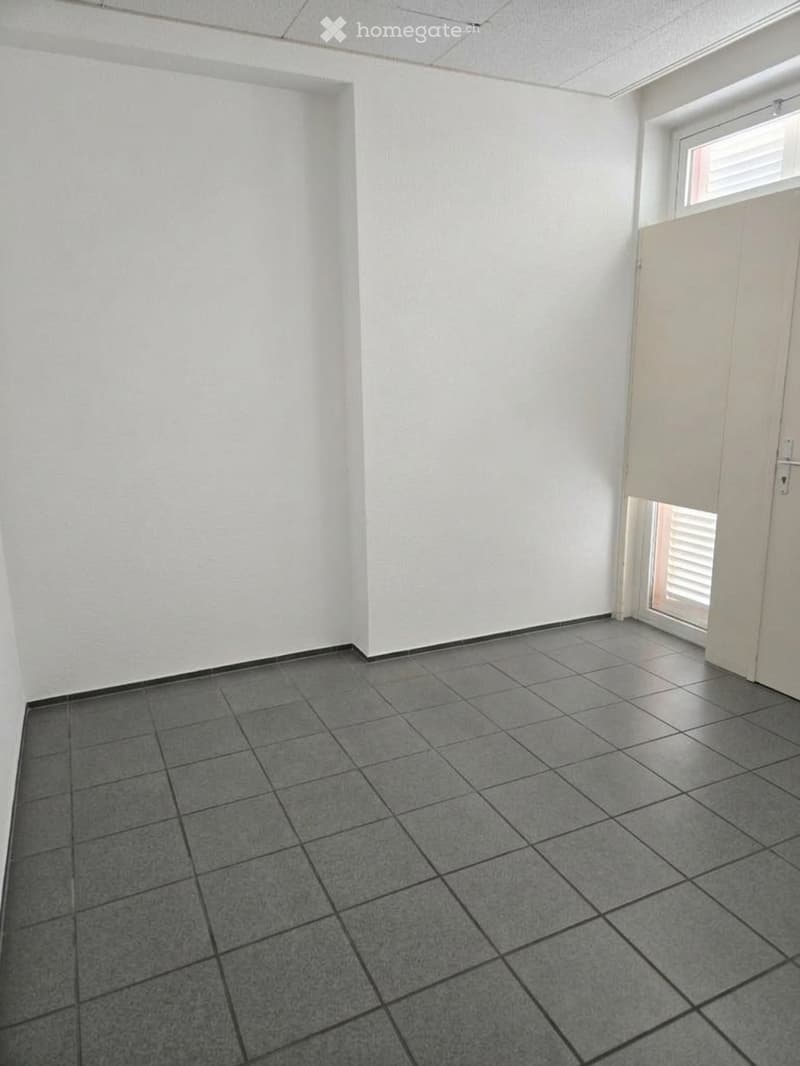 Empty room with white walls, grey tiled floor, and a white door leading to another space.