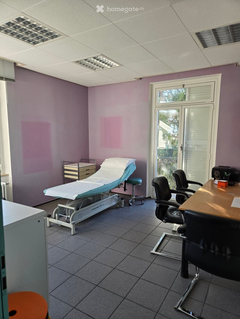Medical examination room with a treatment table, stool, chairs, desk, and cabinet.