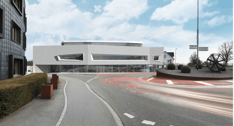 Modern building with a sleek, contemporary design featuring large glass windows and a clean, minimalist facade. The surrounding area includes a landscaped driveway, small sculptures, and neatly trimmed hedges.