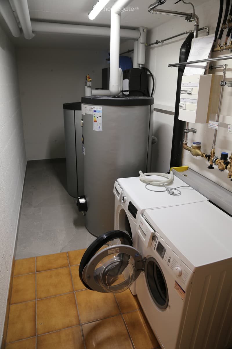 Laundry room with a white Bosch washing machine and a water heater, featuring tiled flooring and exposed pipes.