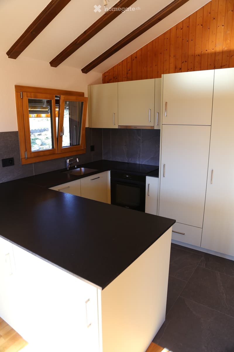 Modern kitchen with white cabinets, black countertops, and a stainless steel sink and oven. Wooden window frame with glass panels allows natural light to enter.