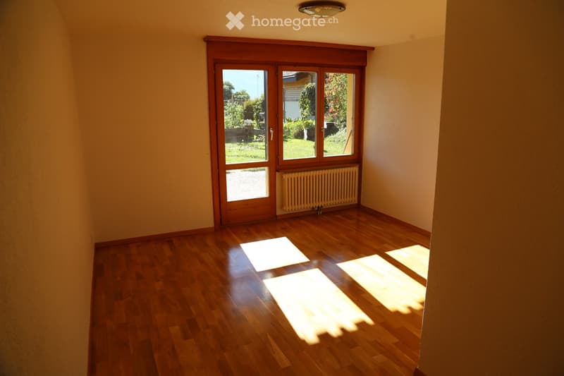 Empty room with wooden flooring, large wooden double doors leading to a garden, radiator, and natural light streaming in.