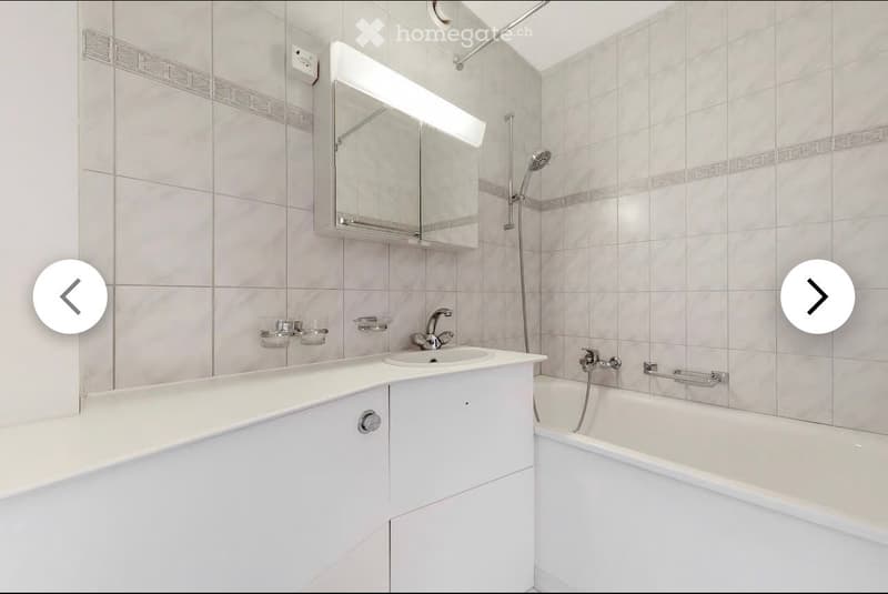 Modern bathroom with white tiles, a sink with a cabinet, a bathtub, a mirror with built-in lighting, and a showerhead.