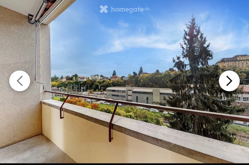 Balcony with metal railing, overlooking a cityscape with buildings, trees, and a clear blue sky.