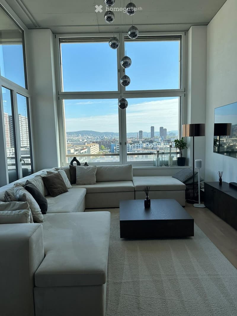 Modern living room with large windows offering a city view, a sectional sofa, coffee table, floor lamp, and decorative items.