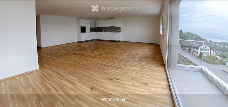 Open-plan living and dining area with wooden flooring, white kitchen cabinets, and large windows offering a scenic view.