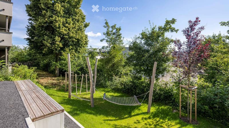 A well-maintained garden with a wooden bench, hammock, and various trees and shrubs.