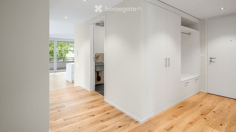 Empty room with light wooden flooring, white walls, built-in white closet, and a small bathroom visible in the background.