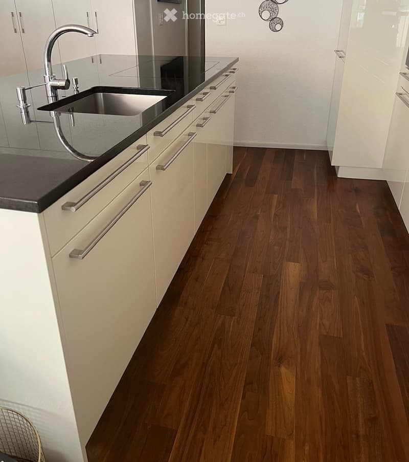 Modern kitchen with white cabinets, dark countertops, and a stainless steel sink. The floor is made of polished hardwood.