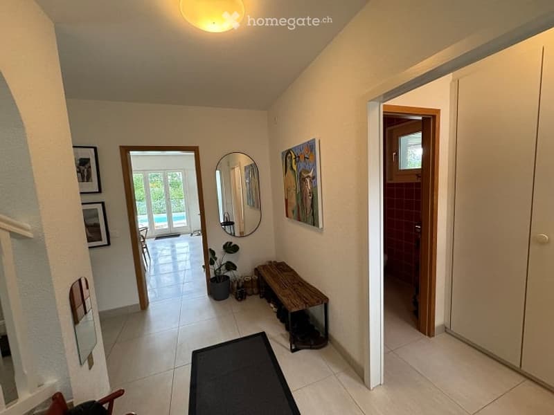 Hallway with tiled floor, white walls, a small bench, a potted plant, and a mirror. Doors lead to other rooms, including a view of a patio area.