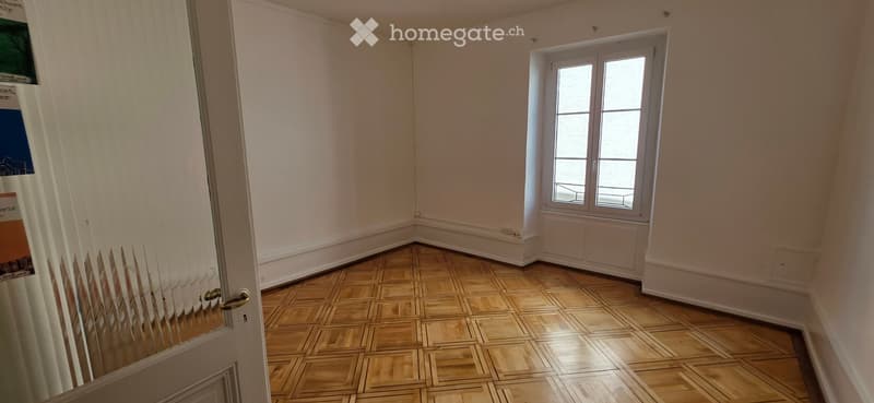 Empty room with wooden parquet flooring, white walls, and a single window with white frame. No furniture or equipment present.
