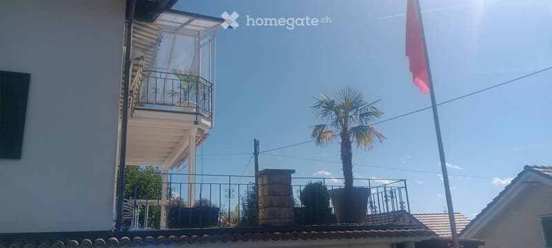 Balcony with metal railing, potted plants, and a clear view of the sky and surrounding area.