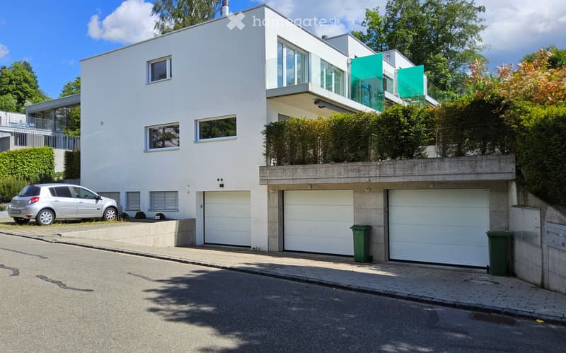 Modern two-story house with white exterior, large windows, and a garage section with three garage doors.