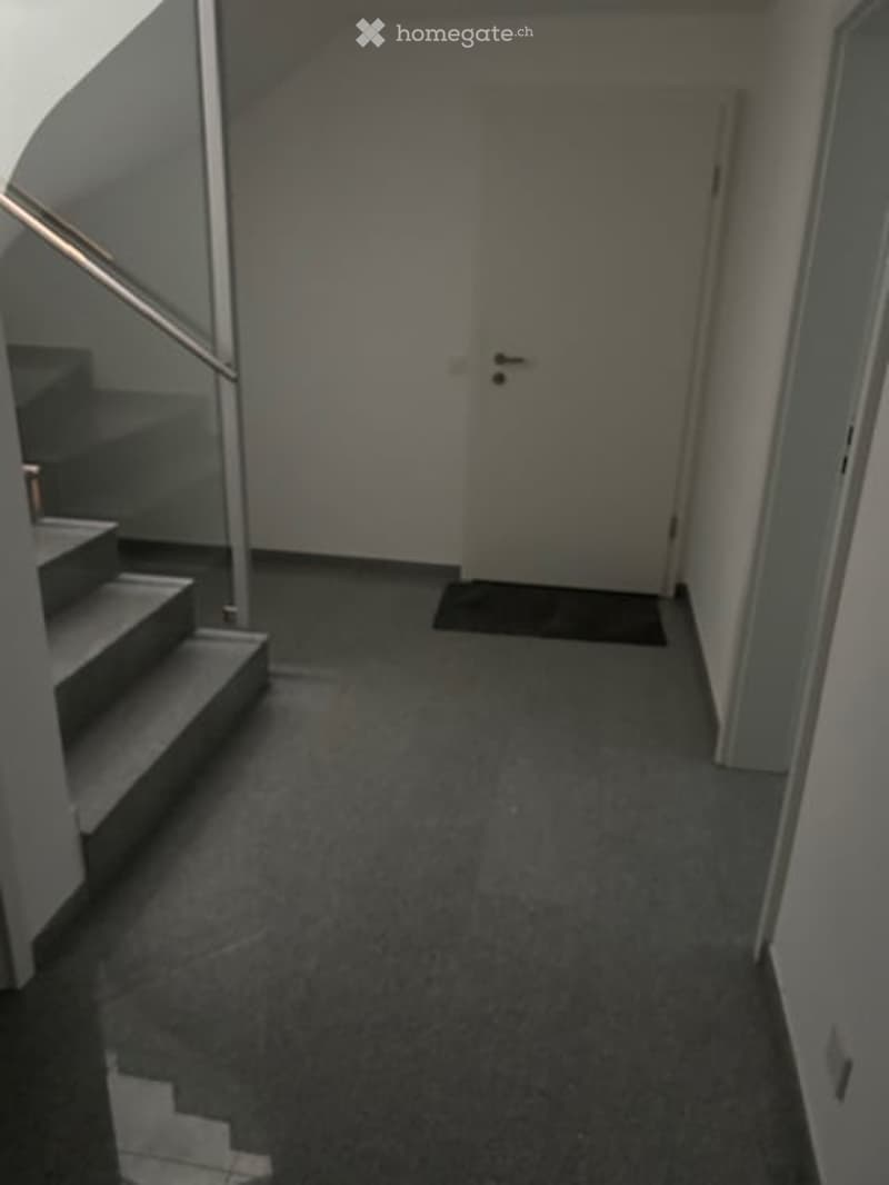 Empty hallway with carpeted floor, a staircase on the left, and a closed door at the end.