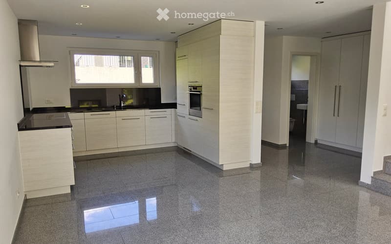 Modern kitchen with white cabinets, black countertops, and a central island. Features include a sink, oven, and range hood, with a large window providing natural light.