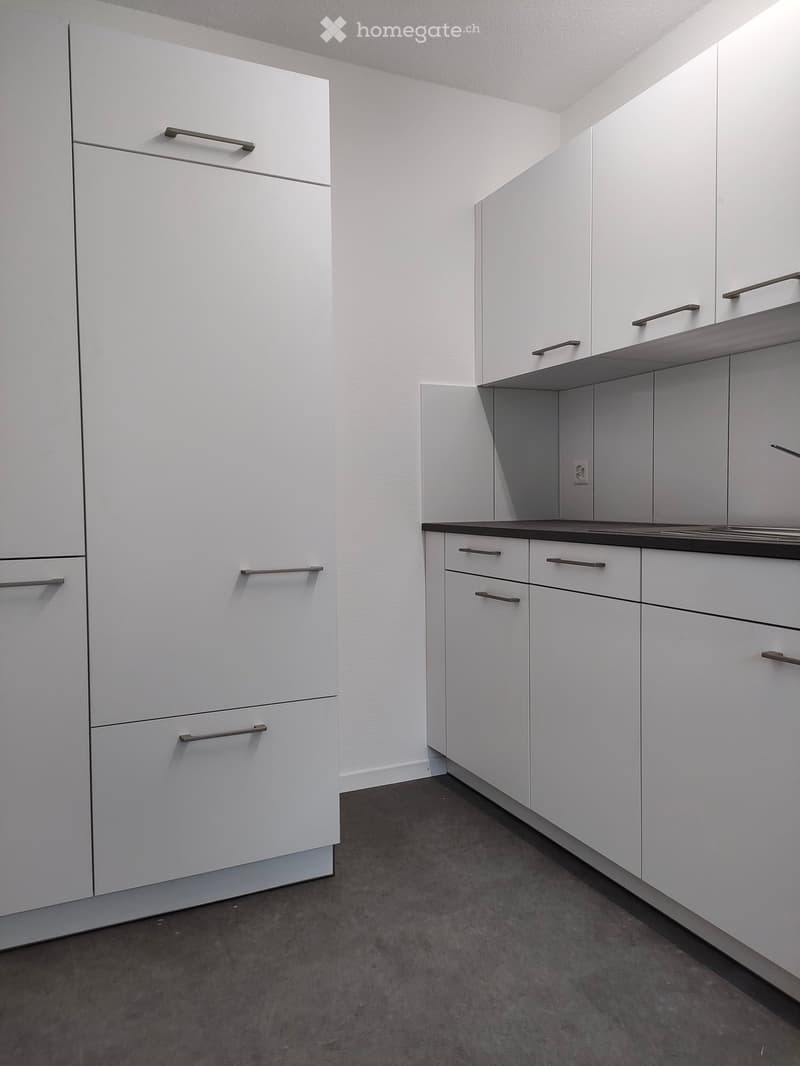Modern, minimalist kitchen with white cabinets, dark countertops, and a dark grey floor. No appliances or furniture are present.