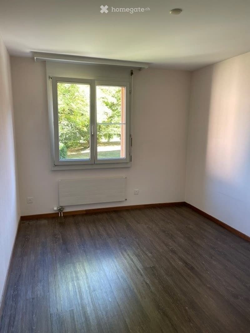 Empty room with wooden flooring, white walls, a window with blinds, and a radiator below the window.