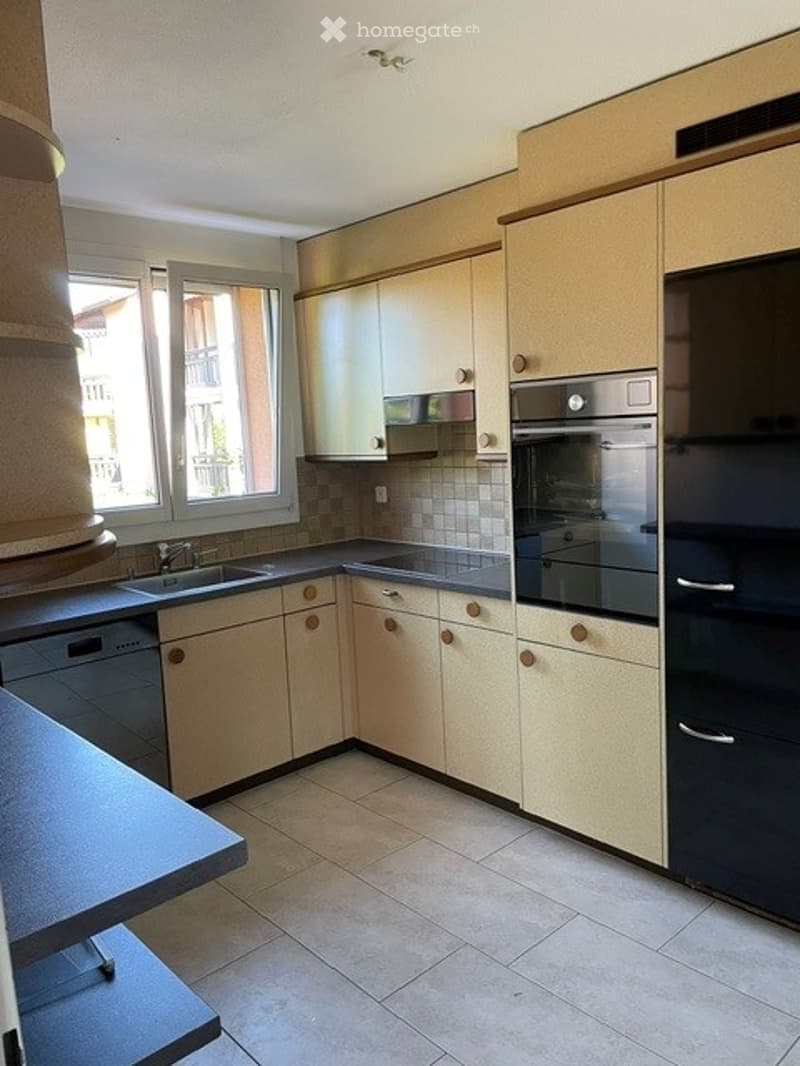 Modern kitchen with light-colored cabinets, stainless steel appliances, and a tiled floor. Features a sink, dishwasher, oven, and refrigerator.