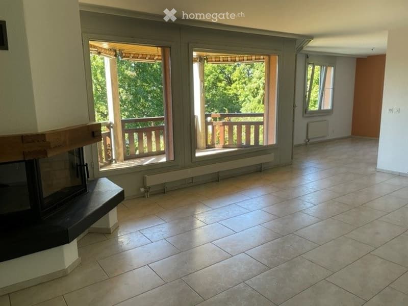 Empty living space with tiled flooring, large windows opening to a balcony, and a fireplace against one wall.