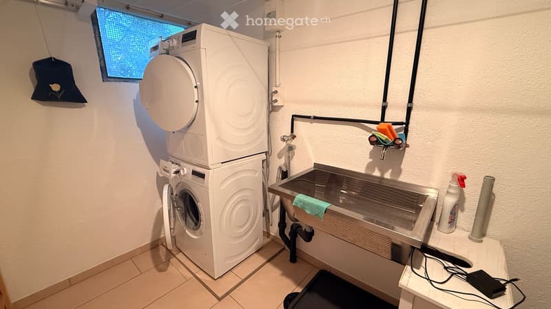 Bathroom with a stacked washing machine and dryer, a sink with a faucet, and a small shelf holding cleaning supplies.